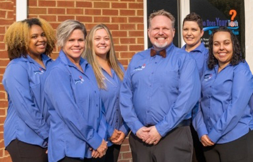 The team at Who Does Your Teeth smiling in matching blue shirts